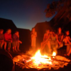 Lagerfeuer. Jugendliche sitzen bei Nacht um ein Feuer. Einer hat eine Gitarre. Vielleicht singen sie oder unterhalten sich.
